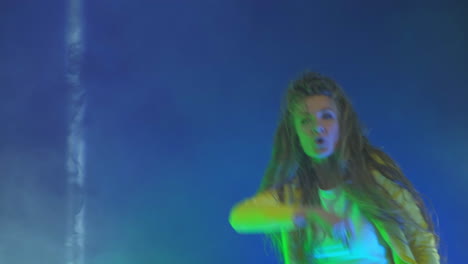 A-funny-woman-in-a-yellow-jacket-jumps-and-dances-energetically-in-the-neon-light-and-smoke